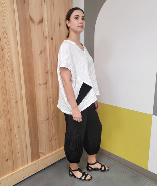 model in a white boxy top with a black panel on the side, worn with a black pant with a dropped cargo pocke at the ankle