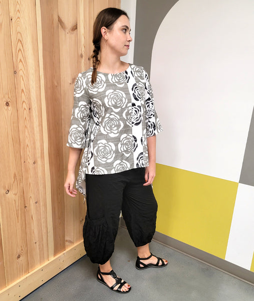 model in a long tunic with an extended back hem, in two dramatic points. tunic is in a striped rose print, worn with a wide leg black cargo pant