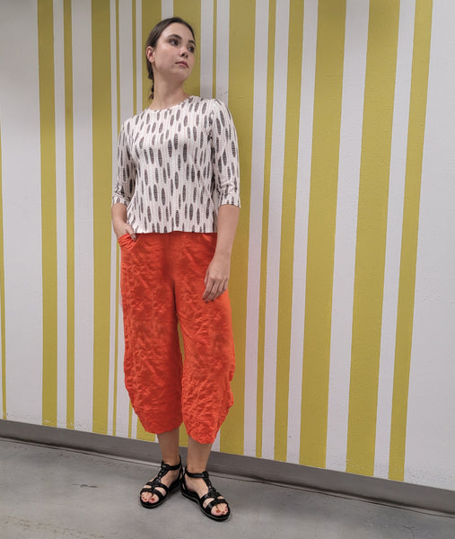 model in a wide leg orange pant with a white pull over tee with a black and orange oval print