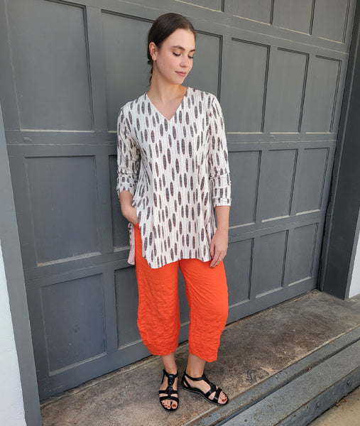 model in a wide leg orange pant with a white pull over vneck tee with a black and orange oval print