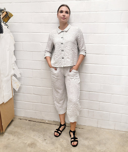 model in a textured white button down blouse and pant with a tiny black dot pattern all over. top has 3/4 sleeves and a double button feature up the placket, pants are wide leg with a tapered ankle