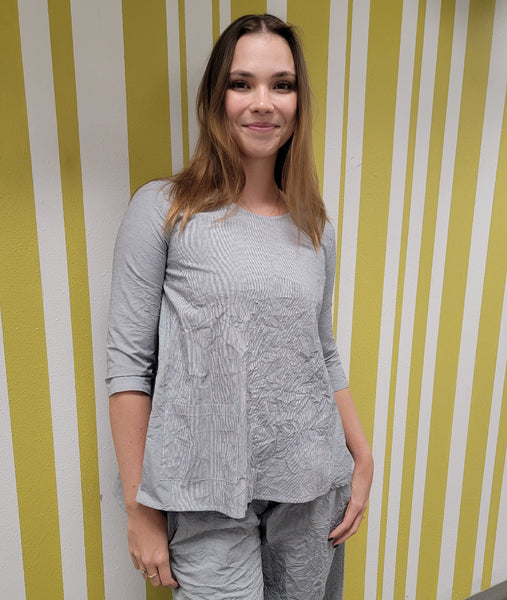 model in a grey and white pinstripe pant with a matching boxy top with a single square pocket at the hip