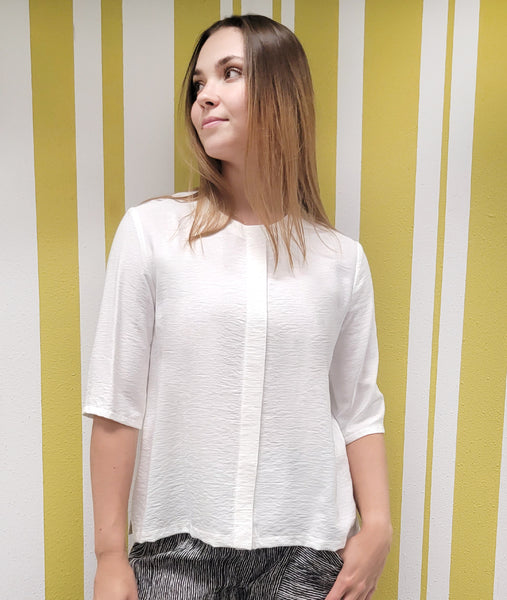 model in a white collarless blouse with 3/4 sleeves and a hidden button placket, worn with a black and white striped pant