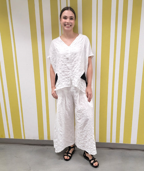 model in a wide leg white pant with front pleats, worn with a matching top with a black contrasting panel on the sides