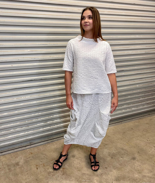 model in a black and white dot print long skirt with a full elastic waist band and large tucks set into the seams with a white top with a tall neckline