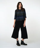 model in a boxy button down blouse with a 3/4 sleeve and twinbutton detail. fabric is striped with varying shades of blues. worn with a wide leg black pant