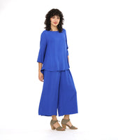 model in a periwinkle pullover top with a round neckline, 3/4 sleeves, and a rounded high-low hem with a flowy godet in the back. worn with a matching wide leg pant with a tall split along the side seam