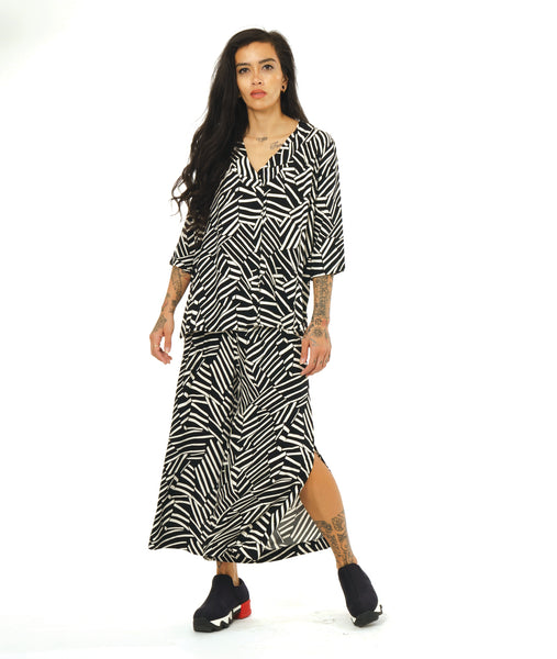 model in a black and white broken stripe print top with 3/4 sleeves, a v-neck, side splits and a center front seam, worn with a matching wide leg pant with a long side split