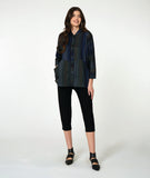 model in a button down blouse with long sleeves, a standing collar, and contrasting directional panels on the body. fabric is striped with varying shades of blues. worn with a slim leg black pant