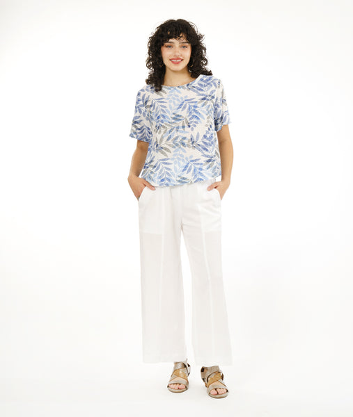 model in a straight leg white pant with a split at the ankle at the center front seam, worn with a boxy pullover top with a rounded neckline in a blue and black leaf print on a white background