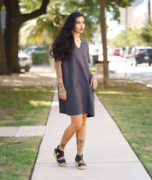 model in a deep grey pullover tunic with a boxy body, cap oversized cap sleeves, a center front seam and pockets set into a horizontal hip seam