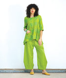 model in a wide leg lime green pant with a tapered ankle, worn with a matching pullover top with a single hip pocket, 3/4 sleeves, a dipped him at either hip and a rounded neckline. Top has an extra large grid print woven in to it