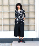 model in a black wide leg pant with an apron style overlay, worn with a black and white print jersey tee with a 3/4 sleeve, rounded neckline and dipped hem on either hip