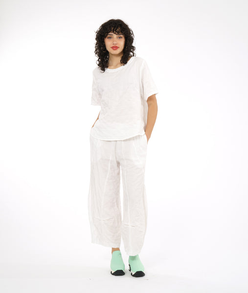 model in a boxy white textured top with a matching pant. pant has a tulip shaped silhouette with a tuck detail at the center front seams, and elastic waistband and pockets