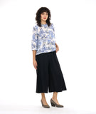 model in a wide leg black pant with a front apron overlay, worn with a white button down blouse with a boxy body, 3/4 sleeves and a blue and black leaf print