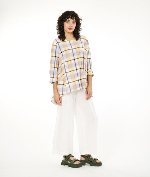 model in a wide leg white pant with a multicolor plaid top with a dipped hem on either hip and rolled sleeves