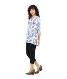 model in a slim, black crop pant with a tunic length white pullover top with a blue and black leaf print. top has squared sets of twin buttons at the placket and two squared pockets and splits at the hip seams