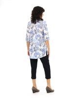 model in a slim, black crop pant with a tunic length white pullover top with a blue and black leaf print. top has squared sets of twin buttons at the placket and two squared pockets and splits at the hip seams