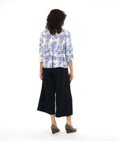 model in a wide leg black pant with a front apron overlay, worn with a white button down blouse with a boxy body, 3/4 sleeves and a blue and black leaf print