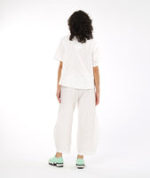 model in a boxy white textured top with a matching pant. pant has a tulip shaped silhouette with a tuck detail at the center front seams, and elastic waistband and pockets