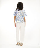 model in a straight leg white pant with a split at the ankle at the center front seam, worn with a boxy pullover top with a rounded neckline in a blue and black leaf print on a white background