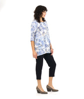 model in a slim, black crop pant with a tunic length white pullover top with a blue and black leaf print. top has squared sets of twin buttons at the placket and two squared pockets and splits at the hip seams