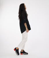 model in a slim leg white pant with a center front seam and a small split at the ankle. worn with a textured black button down blouse with rolled sleeves and a black and white button