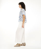 model in a straight leg white pant with a split at the ankle at the center front seam, worn with a boxy pullover top with a rounded neckline in a blue and black leaf print on a white background