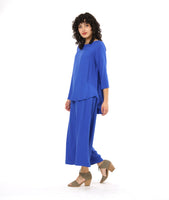 model in a periwinkle pullover top with a round neckline, 3/4 sleeves, and a rounded high-low hem with a flowy godet in the back. worn with a matching wide leg pant with a tall split along the side seam