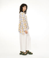 model in a wide leg white pant with a multicolor plaid top with a dipped hem on either hip and rolled sleeves