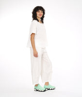 model in a boxy white textured top with a matching pant. pant has a tulip shaped silhouette with a tuck detail at the center front seams, and elastic waistband and pockets