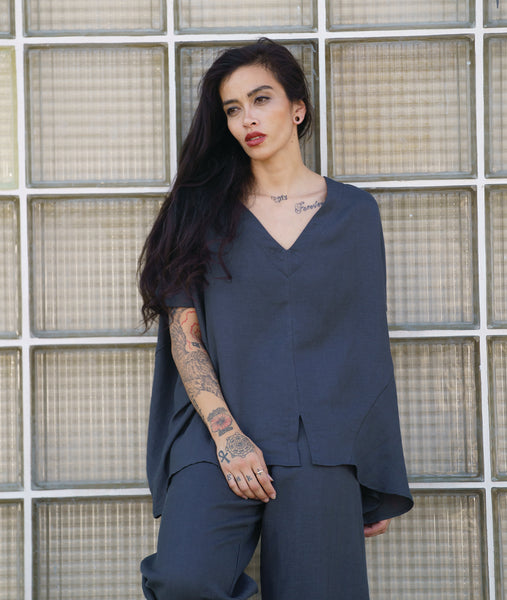 model in a boxy cocoon style pullover blouse in a deep grey. top has a v-neck, short sleeves, angled panels and a split at the center front hem. worn with a matching wide leg pant