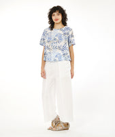 model in a straight leg white pant with a split at the ankle at the center front seam, worn with a boxy pullover top with a rounded neckline in a blue and black leaf print on a white background