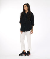 model in a slim leg white pant with a center front seam and a small split at the ankle. worn with a textured black button down blouse with rolled sleeves and a black and white button