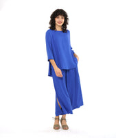 model in a periwinkle pullover top with a round neckline, 3/4 sleeves, and a rounded high-low hem with a flowy godet in the back. worn with a matching wide leg pant with a tall split along the side seam