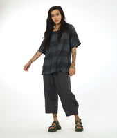 model in a wide leg dark grey pant with a tulip shaped silhouette, and a matching dark grey pullover top with a large rounded neckline, elbow length raglan sleeve, and a large checkered print woven into the fabric