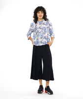 model in a wide leg black pant with a front apron overlay, worn with a white button down blouse with a boxy body, 3/4 sleeves and a blue and black leaf print