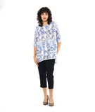 model in a slim, black crop pant with a tunic length white pullover top with a blue and black leaf print. top has squared sets of twin buttons at the placket and two squared pockets and splits at the hip seams