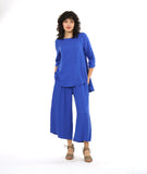 model in a periwinkle pullover top with a round neckline, 3/4 sleeves, and a rounded high-low hem with a flowy godet in the back. worn with a matching wide leg pant with a tall split along the side seam