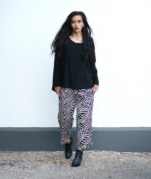 model in a black and white broken stripe print straight leg pant with a small split at the ankle front, worn with a black twill top with a false placket, long sleeves and a rounded neckline