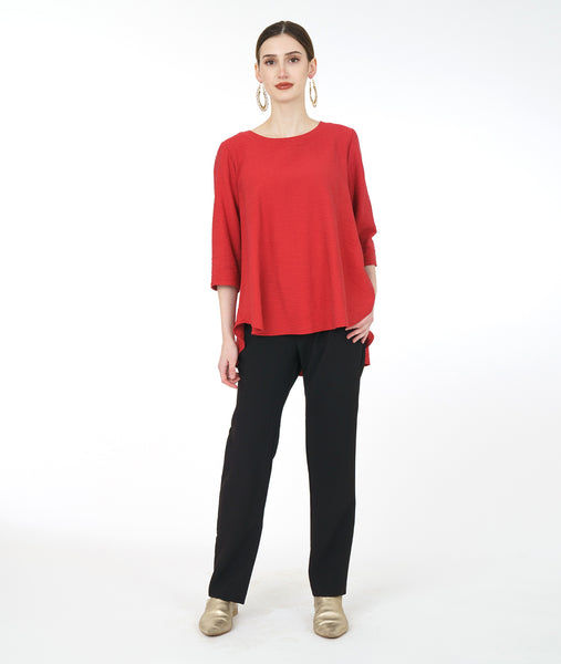 model in a slim black pant with a red pull over top with 3/4 sleeves, a round neckline, and a rounded high low hem with a full flowy body in the back