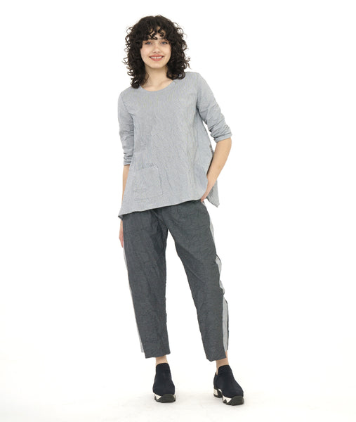 model in a grey and white pinstriped top with a crush texture to it. top has a boxy body with a draped hem on either side. worn with a matching pant with a grey and black stripe with a white and grey panel on the side in a tuxedo stripe style