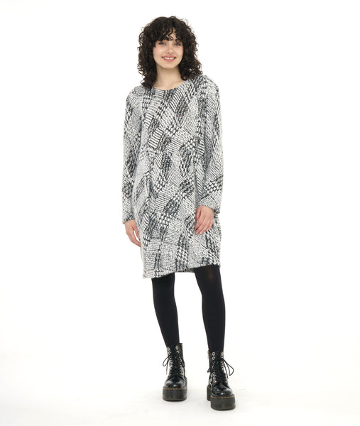 model in a black and white knee length, long sleeve tunic in a black and white print, tunic has a soft round neckline and pleats at the waist. worn with black tights and boots.