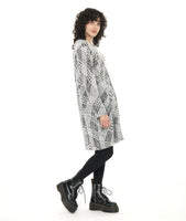 model in a black and white knee length, long sleeve tunic in a black and white print, tunic has a soft round neckline and pleats at the waist. worn with black tights and boots.
