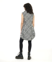 model in a sleeveless black and white plaid tunic with an oversized cowl neck, full length princess seams, and dramatic pleating at the hip seams. worn with black leggings and boots
