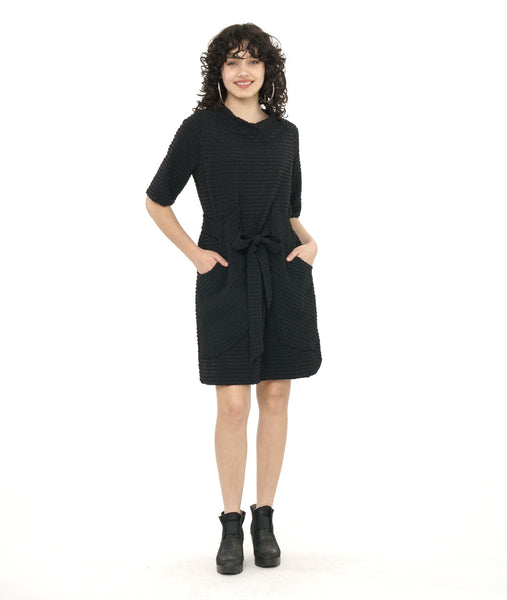 model in a textured black shift dress with a matching tie belt, deep exterior pockets, and elbow length raglan sleeves