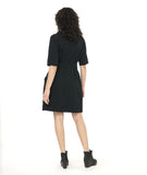 model in a textured black shift dress with a matching tie belt, deep exterior pockets, and elbow length raglan sleeves