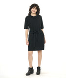 model in a textured black shift dress with a matching tie belt, deep exterior pockets, and elbow length raglan sleeves