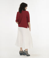 model in a wide leg white pant with an apron style panel overlay, worn with a brick red button up top with 3/4 sleeves and a round neckline