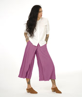 model in a wide leg dusty rose pant with an apron style panel overlay, worn with a white button up top with 3/4 sleeves and a round neckline